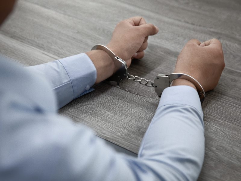 A selective focus shot of male hands in handcuffs on a wooden table